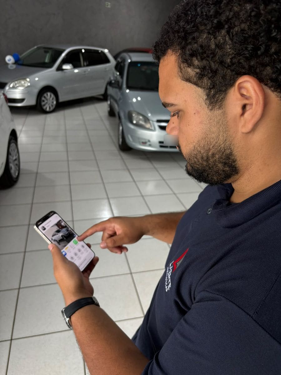 Dono de loja de carros mandando as fotos de um carro pelo celular, dentro da loja